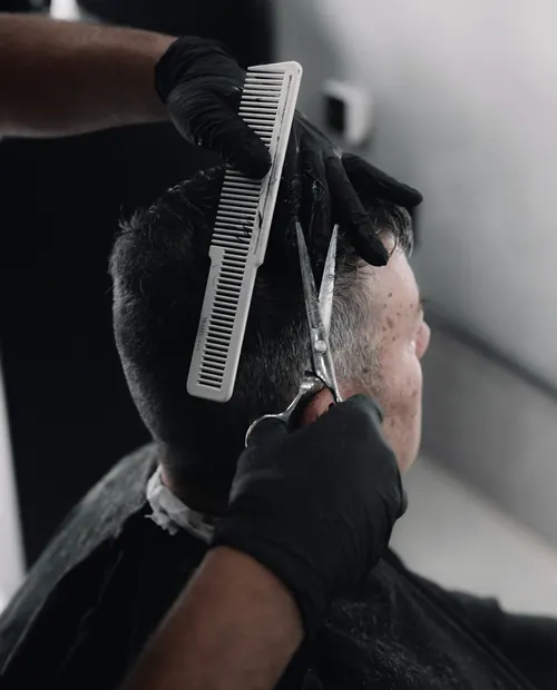 Barber w czarnych rękawiczkach strzyże nożyczkami na grzebieniu