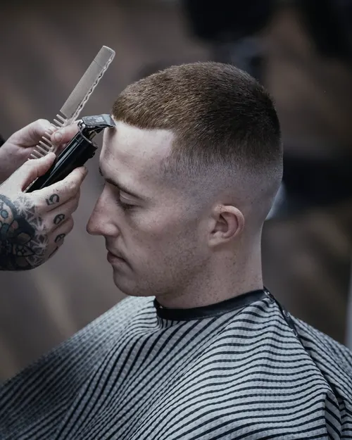 Klient z krótko ściętymi włosami i wysokim cieniowaniem, barber poprawia maszynką linię nad czołem