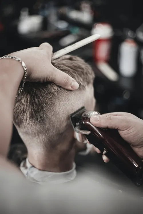 Ręce barbera cieniują maszynką boki głowy klienta