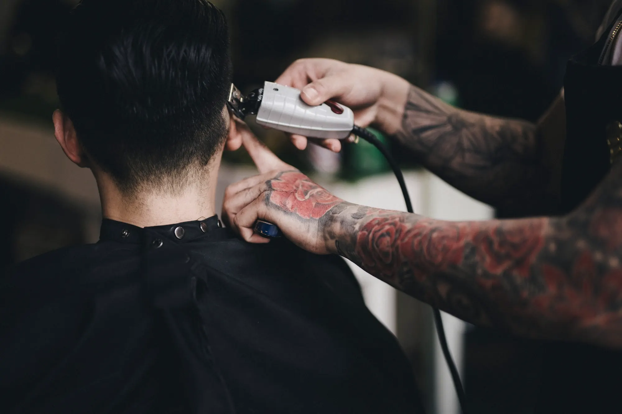 Barber z wytatuowanymi rękami podcina maszynką kark klienta